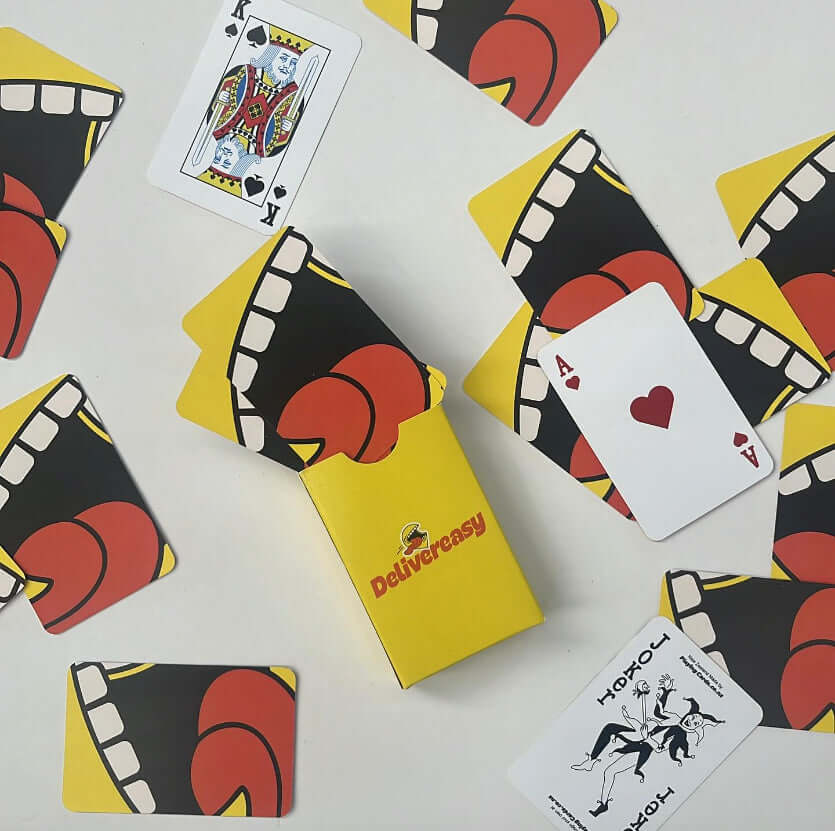 Custom poker sized playing cards with vibrant designs and a branded yellow box, featuring jokers, aces, and king on display.